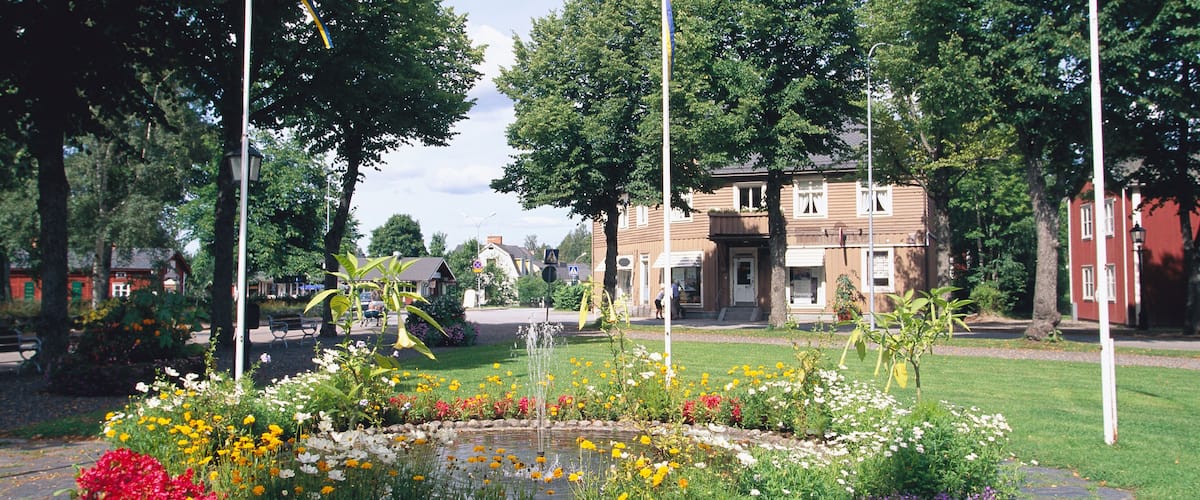 A park with a flower bed, a fountain, and a building in the background.