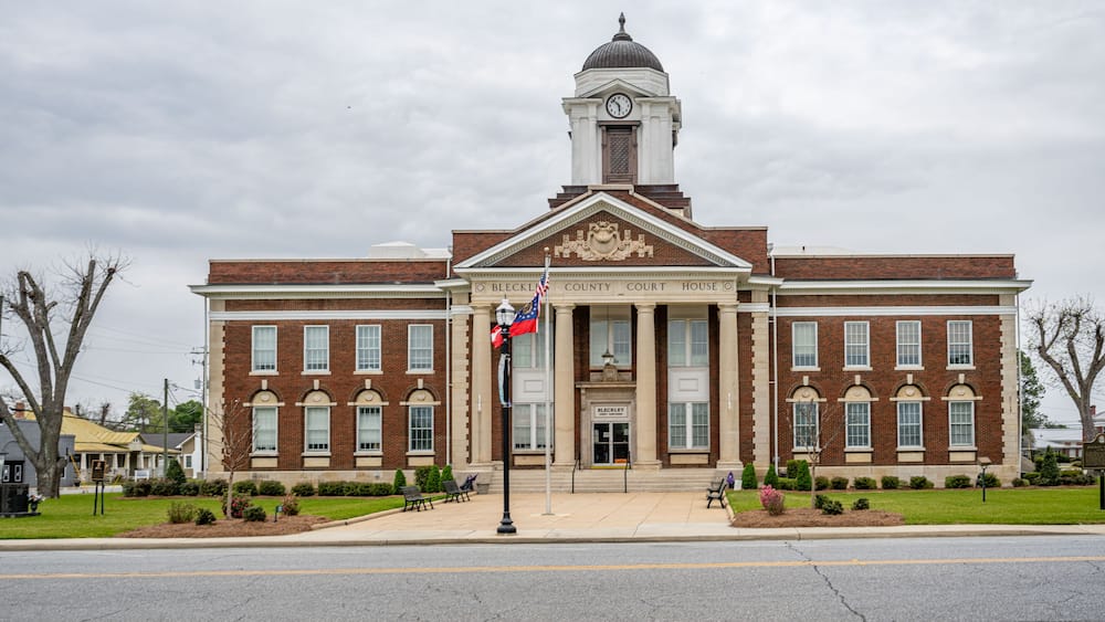 A brick courthouse with a clock tower, a flag, and a well-maintained lawn.