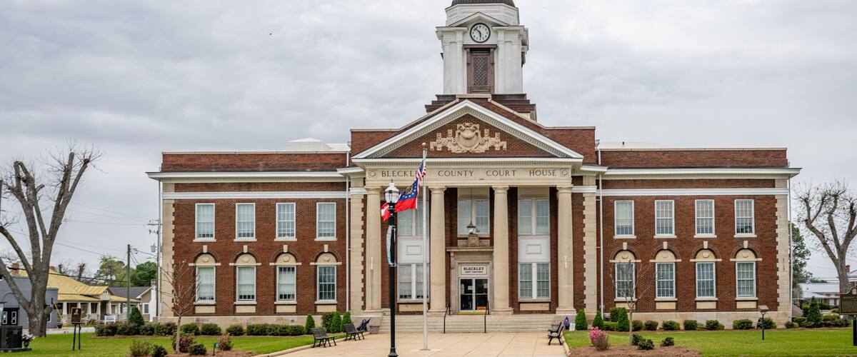 A brick courthouse with a clock tower, a flag, and a well-maintained lawn.