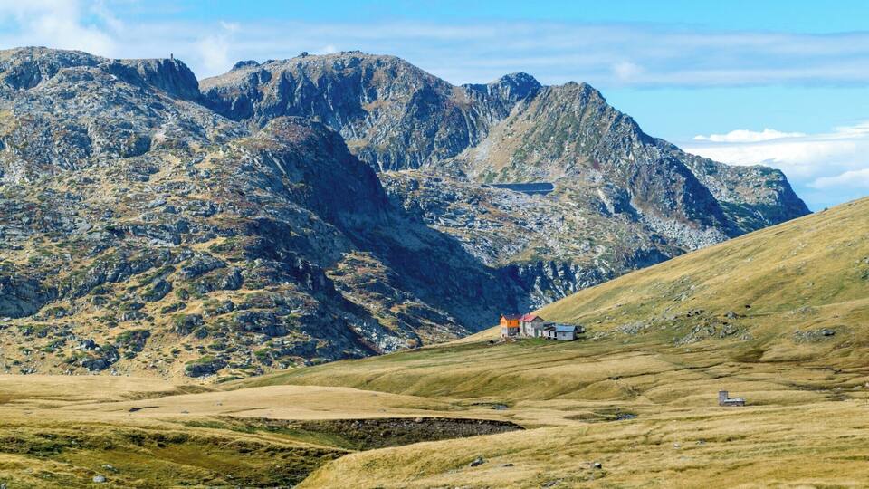A mountainous landscape with a small house and a path leading up to it.