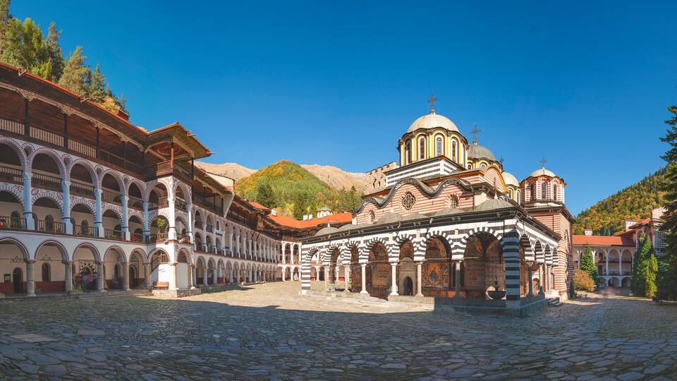 A historic building with a dome and arches, surrounded by cobblestone streets and trees.