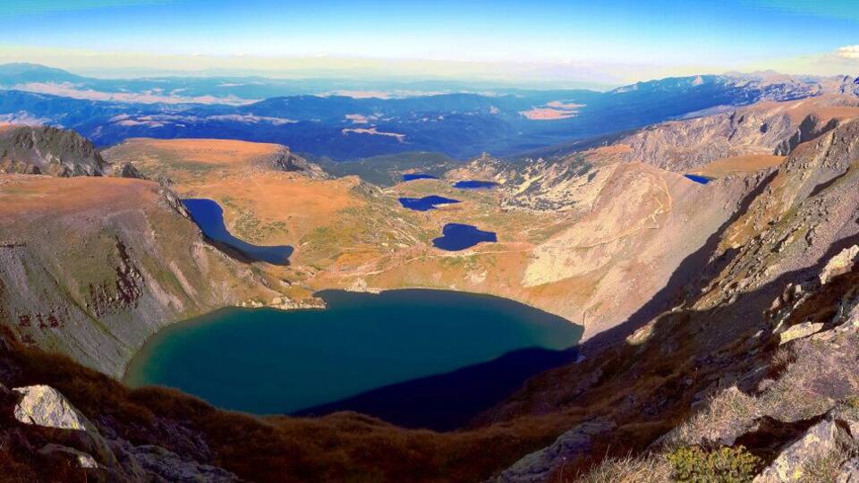 A mountainous landscape with a large lake surrounded by rocky terrain and distant mountain ranges.