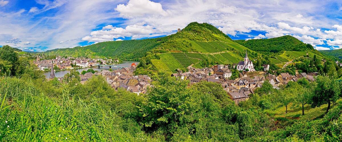 A picturesque village nestled in a valley with lush greenery, a prominent church, and a bridge over a river.