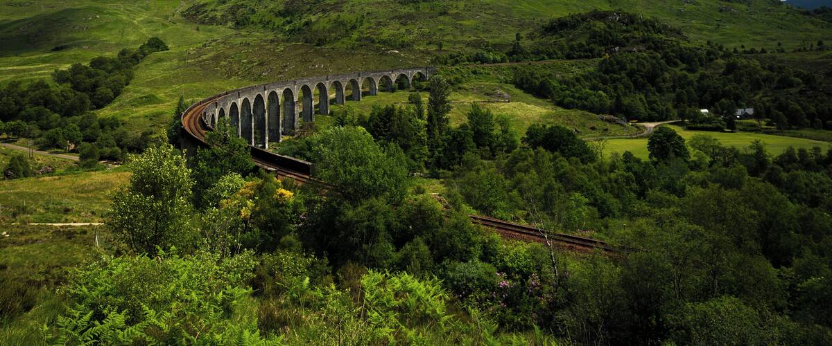 A railway viaduct in a lush green valley with rolling hills in the background.