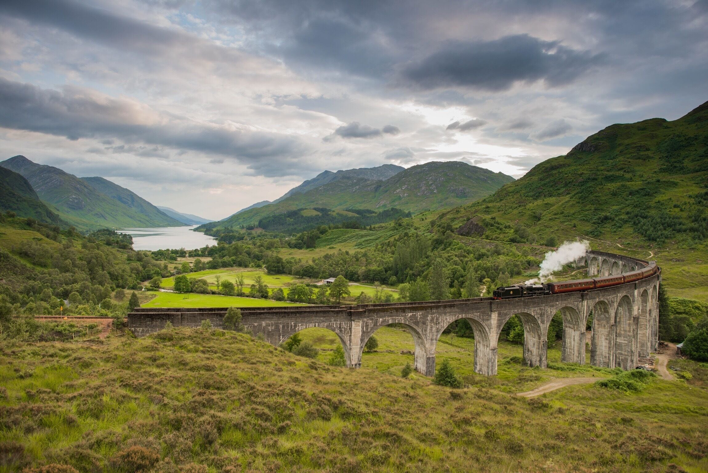 A railway viaduct in a lush valley with a lake in the background.