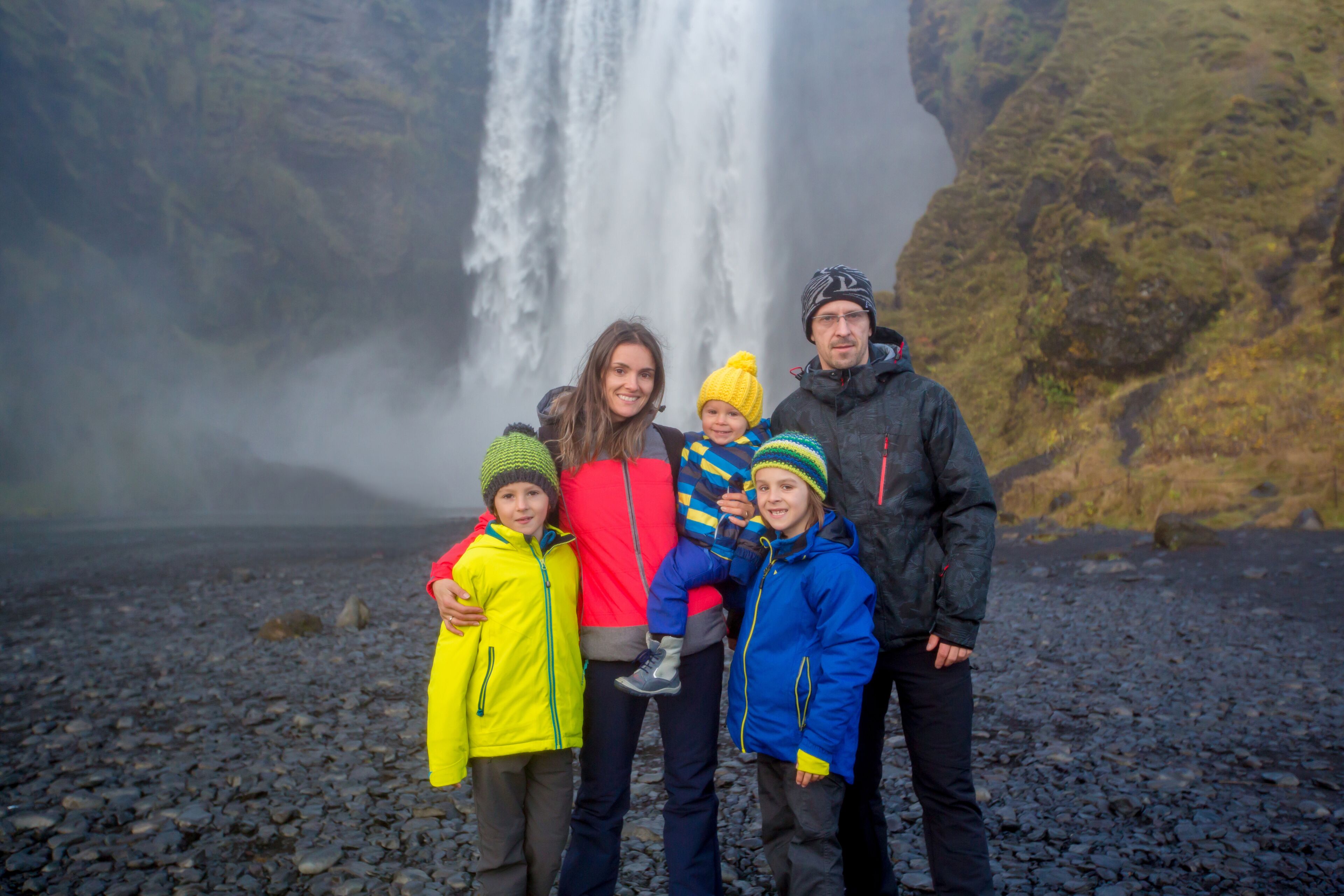 Uma família em frente a uma cachoeira, com terreno rochoso ao fundo.