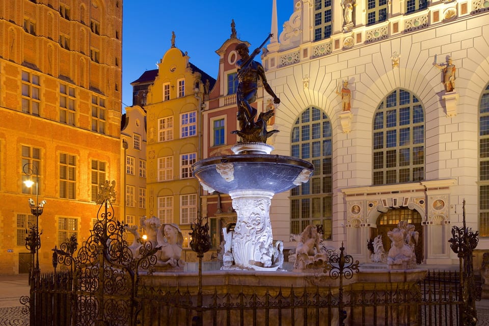 A historic fountain with statues in an urban square surrounded by ornate buildings.