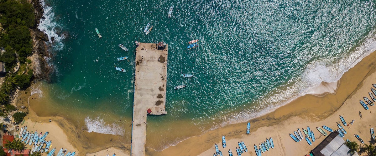 An aerial view of a beach with numerous boats lined up along the shore and a pier extending into the water.