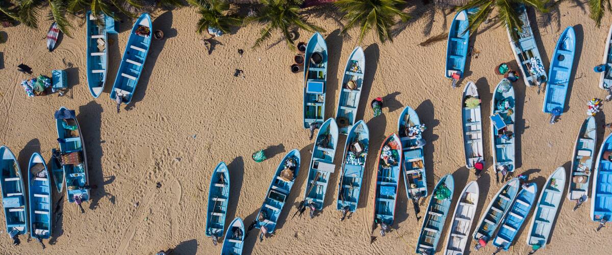 A beach with numerous blue boats lined up and people walking around.