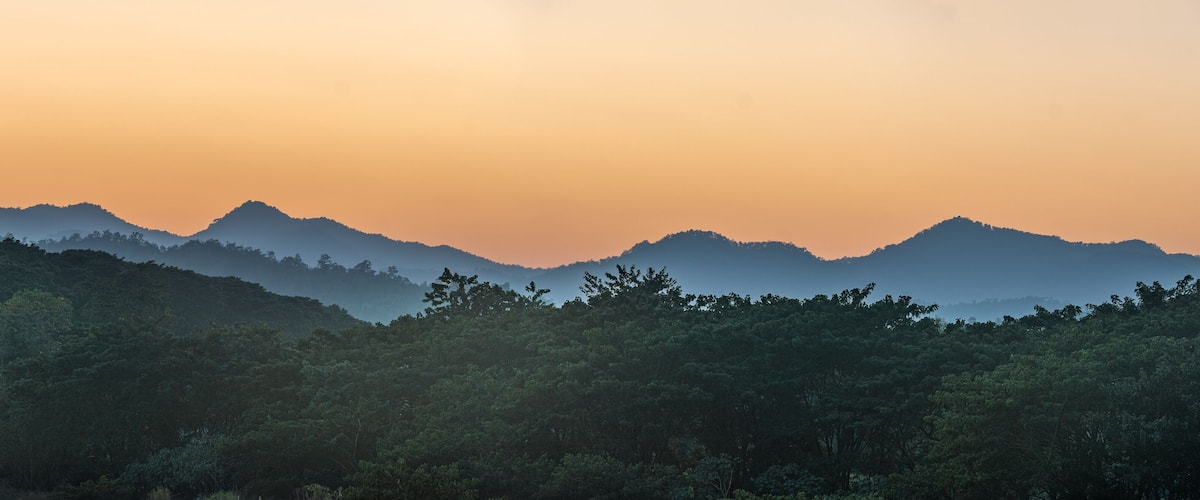 A mountain range with dense forest at the base during sunset.
