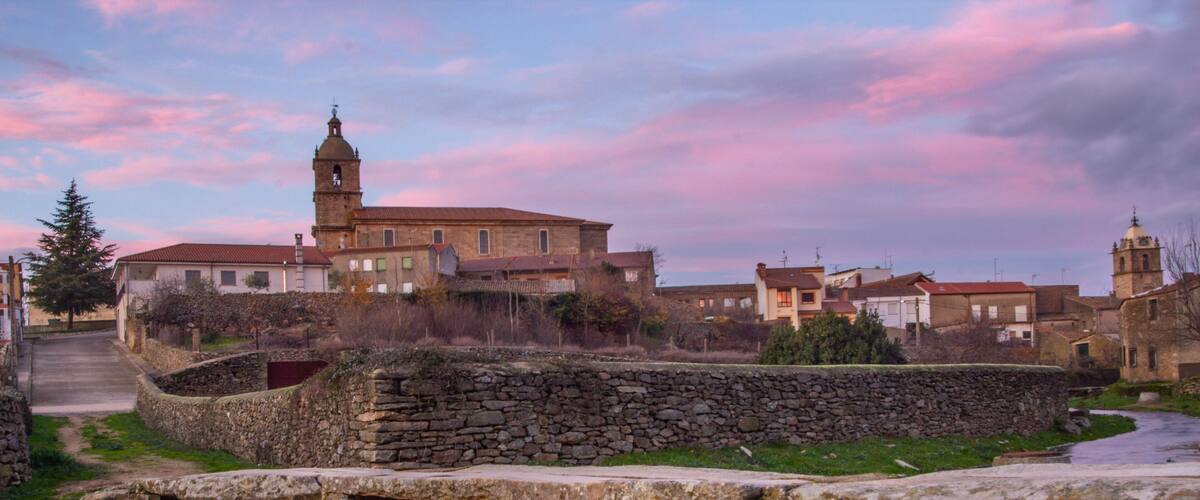 A stone bridge over a river, surrounded by historic buildings and a church with a bell tower.