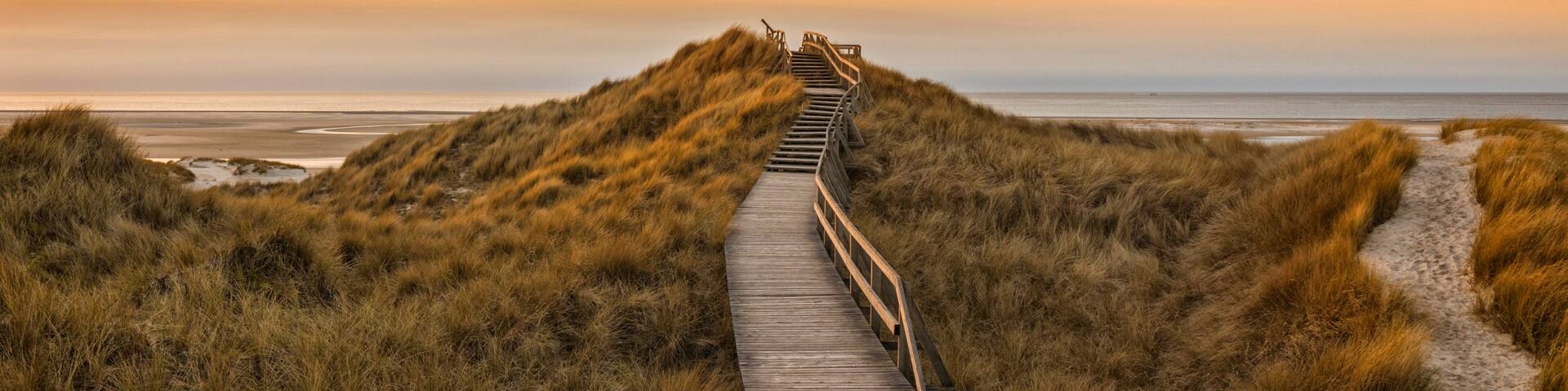 Wooden path and stairs crossing the dunes to the beach of Norddorf, Amrum, in sunset