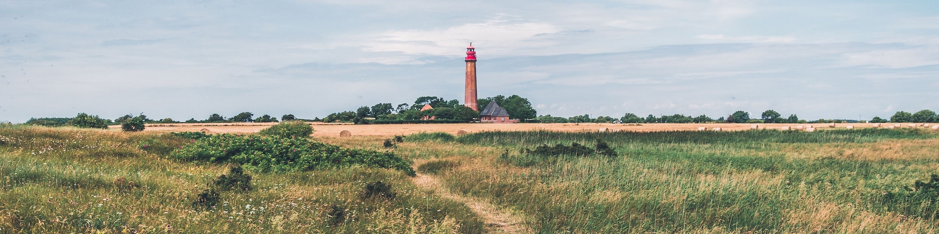 A lighthouse on a grassy hill with a clear sky.