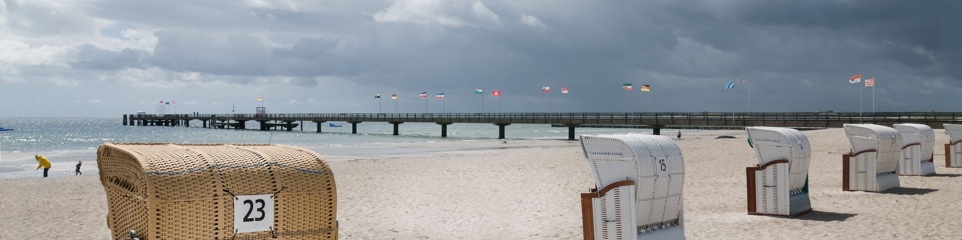 Empty beach chairs on the Baltic Sea beach and pier with the flags of German constituent states and cities. Grossenbrode, Schleswig- Holstein, Germany