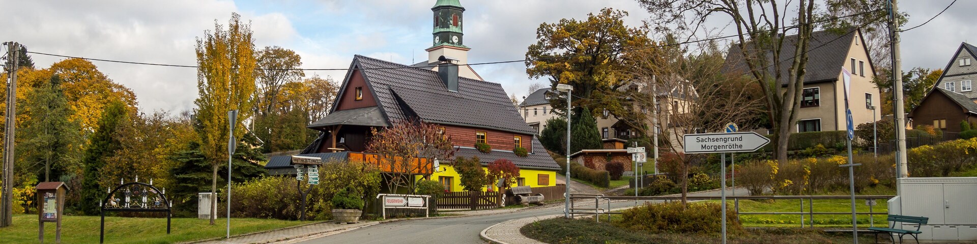 Uma rotatória de paralelepípedos, com uma igreja e casas ao fundo.