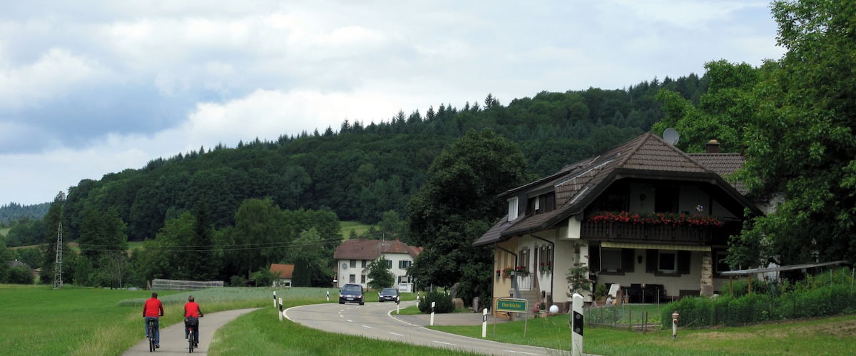A rural road with cyclists, a restaurant, and a forested hill.