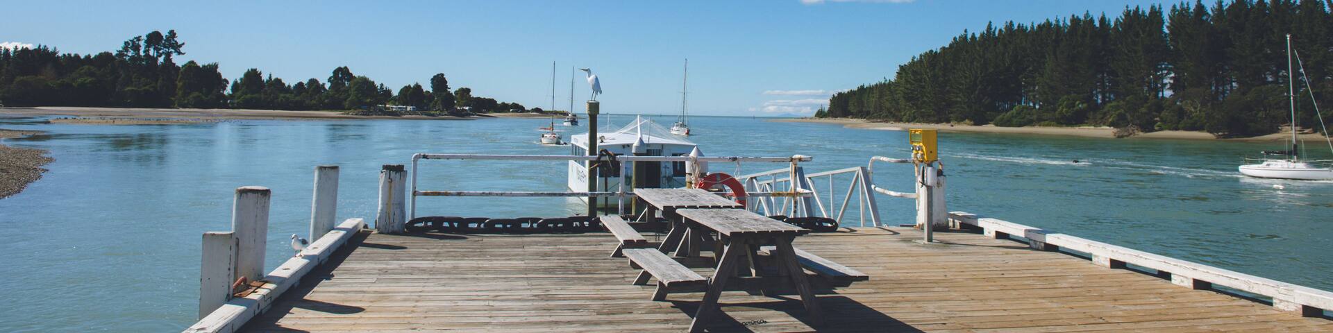 A wooden pier extending into calm waters with boats docked, a clear sky, and a forested shoreline.