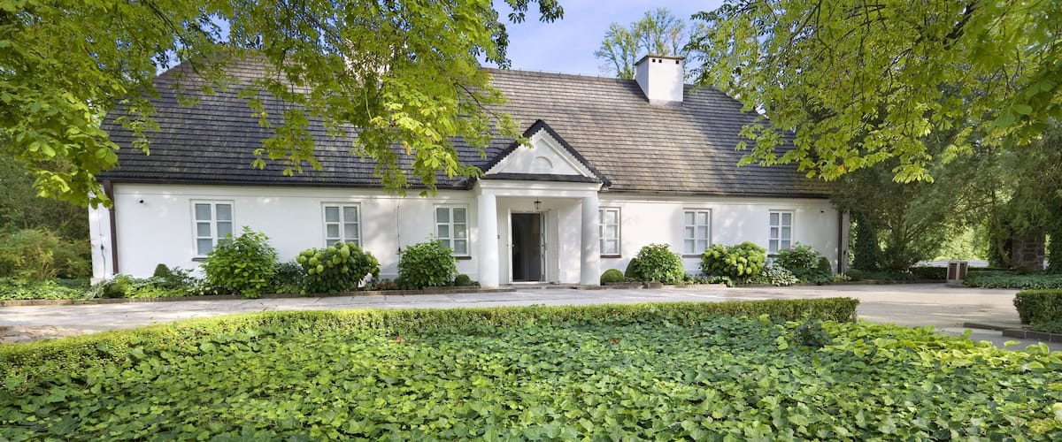 A white house with a dark roof, surrounded by lush greenery and a well-maintained garden.