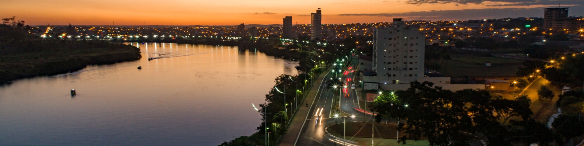 A river with a bridge, a road with traffic, and city lights at dusk.
