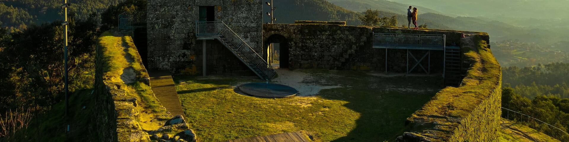 A stone tower with a staircase, surrounded by a grassy area and a view of distant mountains.