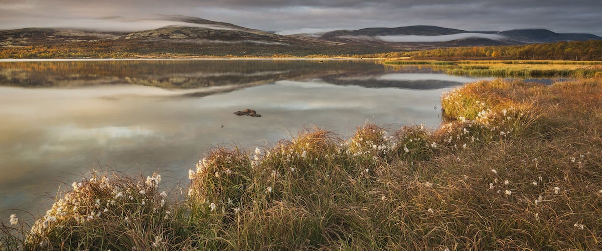 A calm lake with surrounding hills and autumn foliage.