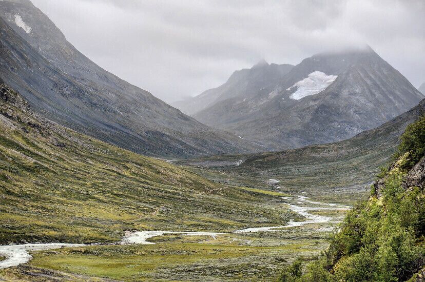 A mountainous valley with a river, snow-capped peaks, and lush greenery.
