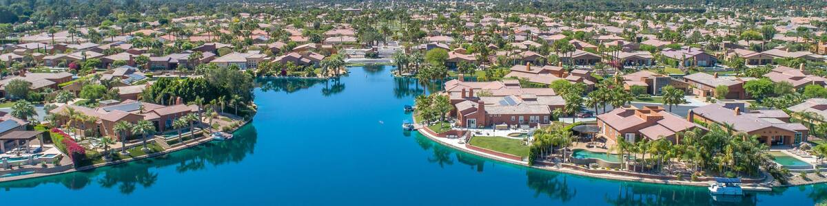 A residential area with a large body of water, surrounded by houses and palm trees, with mountains in the background.