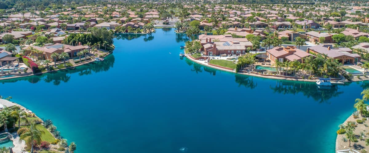 A residential area with a large body of water, surrounded by houses and palm trees, with mountains in the background.