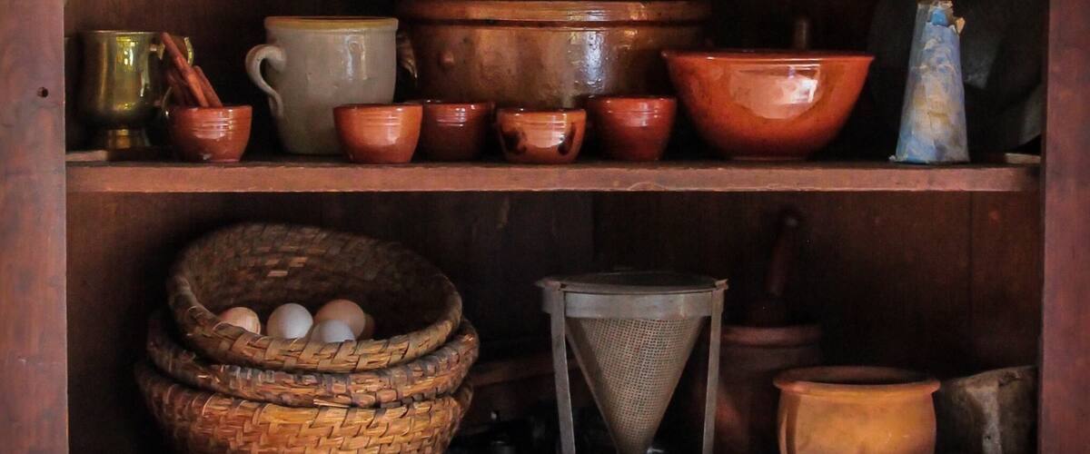 A wooden shelf with various ceramic items, including bowls, cups, and a basket with eggs.