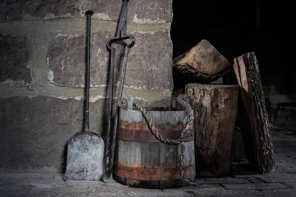A rustic stone wall, a wooden bucket, a shovel, and a log.