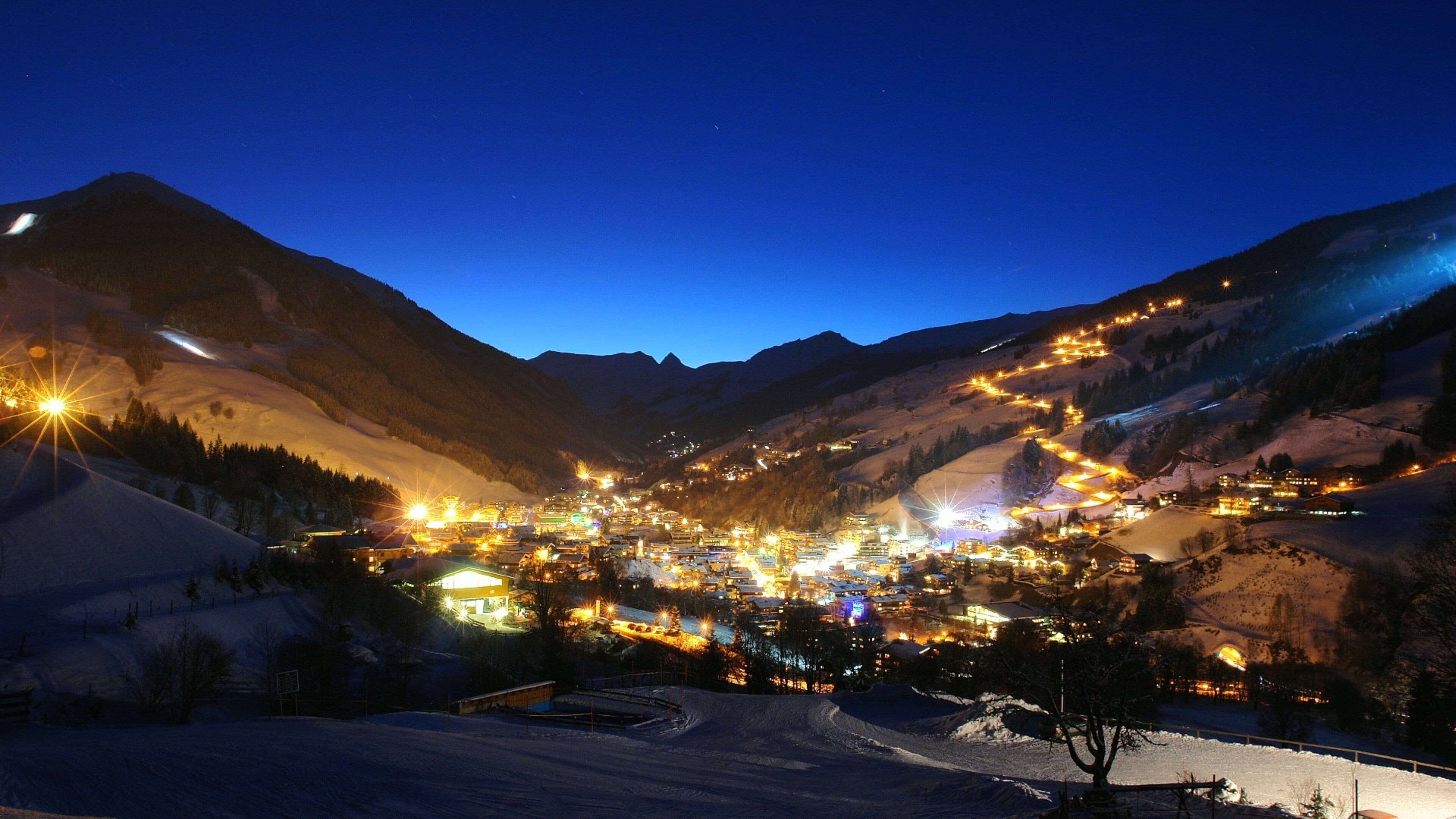 A snow-covered mountain village at night with illuminated buildings and winding roads.
