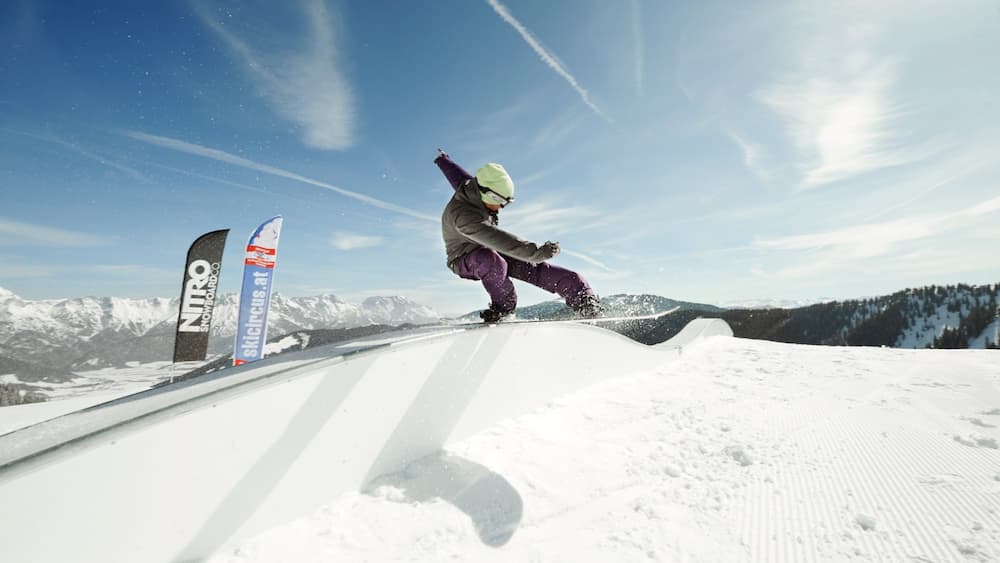 Un snowboardeur effectuant une figure sur une pente enneigée, avec des montagnes en arrière-plan.