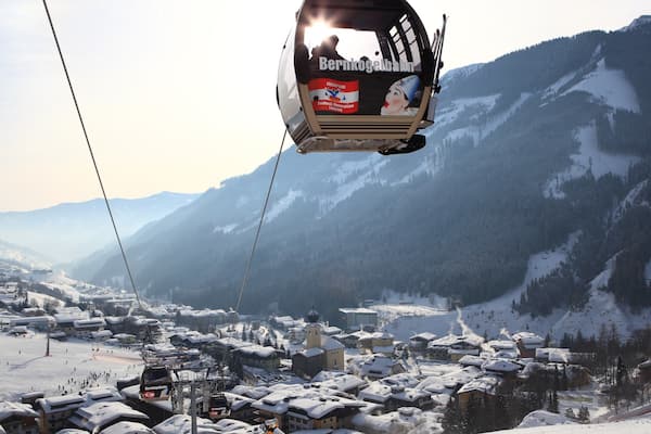 Eine Seilbahn in einem verschneiten Bergdorf mit Gebäuden und bewaldeter Landschaft.