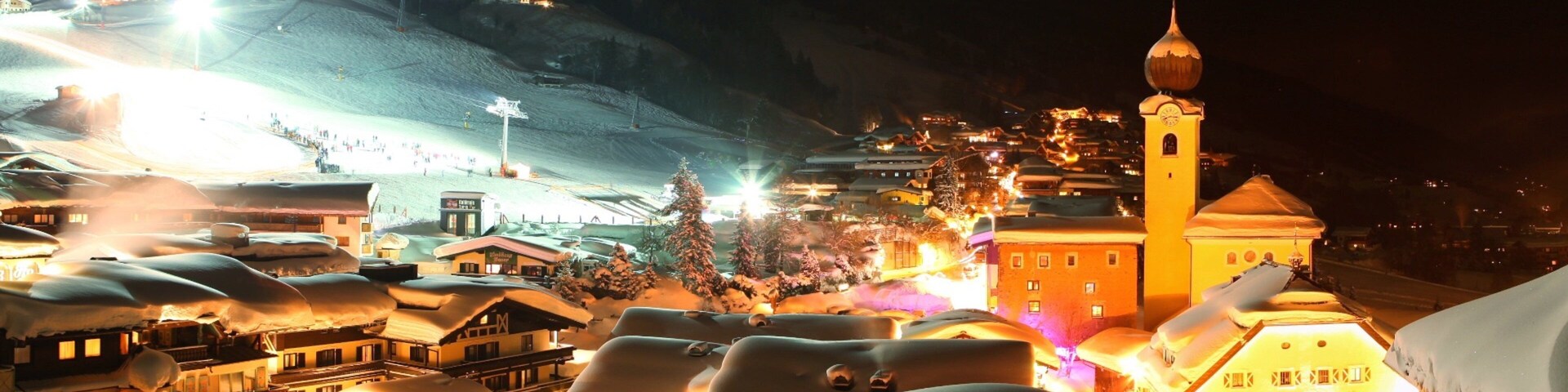 Un pueblo cubierto de nieve por la noche con edificios iluminados y una imponente torre de iglesia.