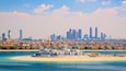 A coastal cityscape with a prominent marina, a sandy beach, and a skyline featuring modern skyscrapers.
