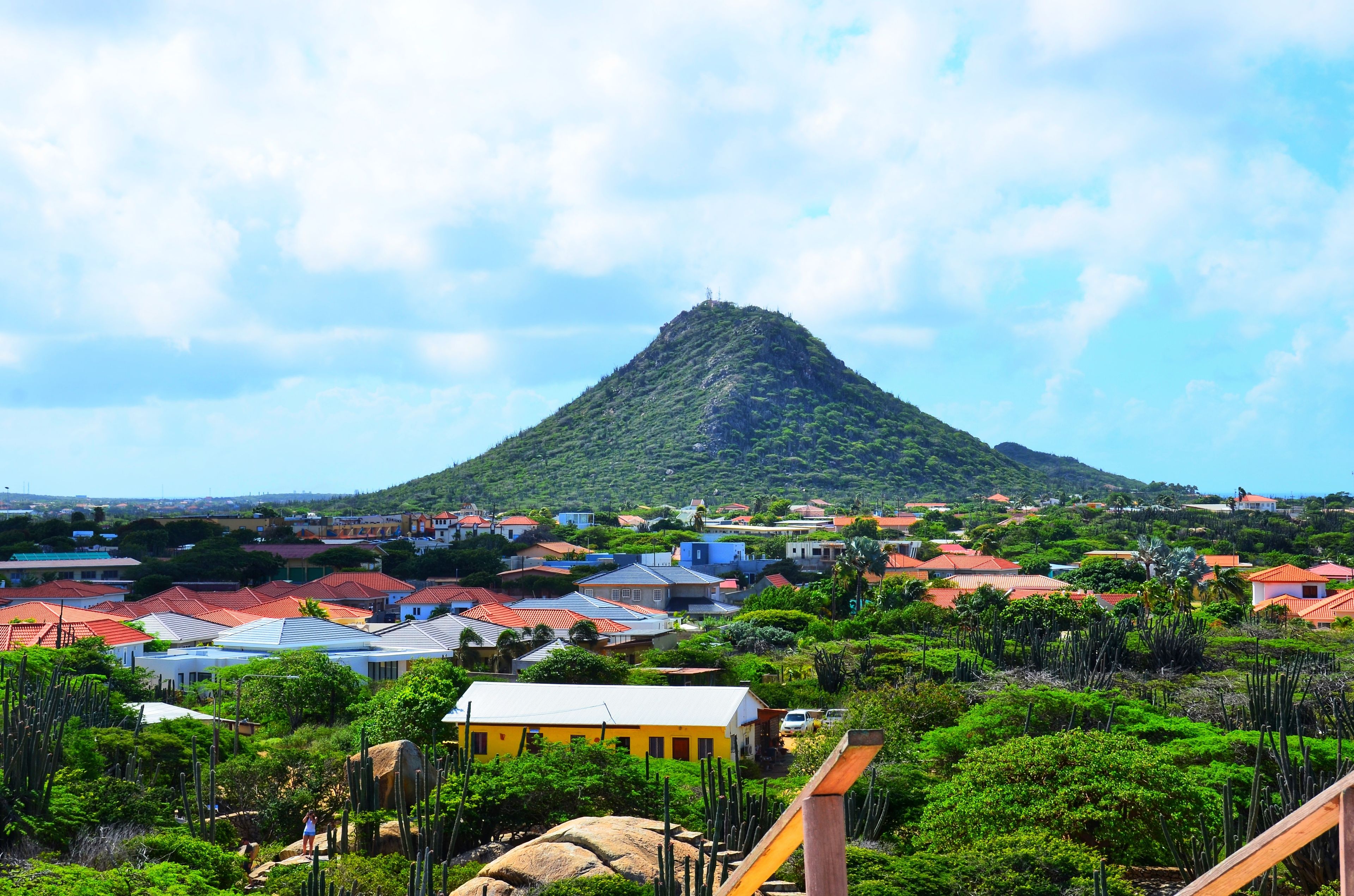 A town with red-roofed houses, a green hill, and a clear sky.