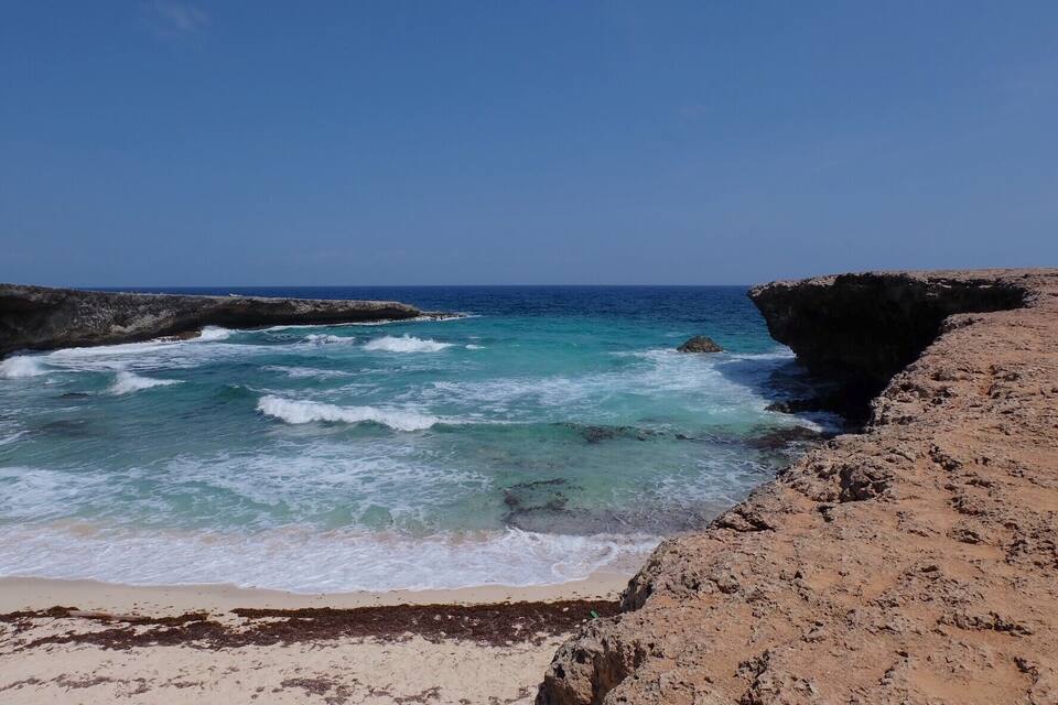 A rocky coastline with clear turquoise waters and a sandy beach.
