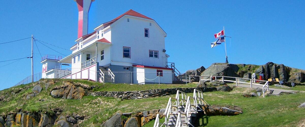 A lighthouse with a red and white tower, a white building with a red roof, and a flagpole with two flags.