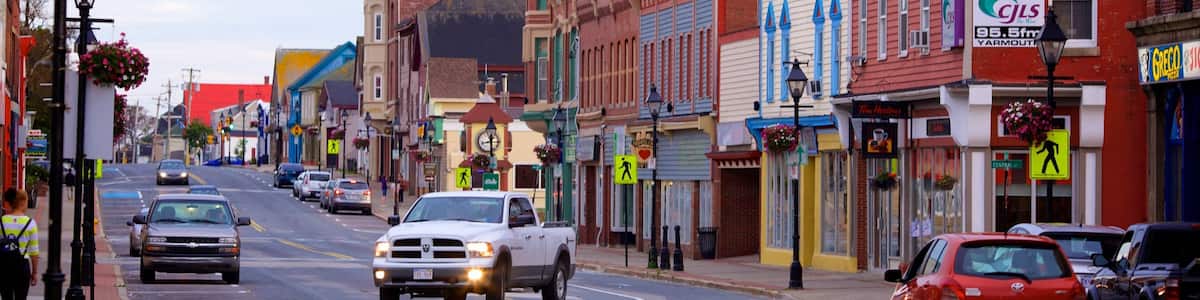 A street lined with colorful buildings, a white truck driving down the road, and various storefronts.