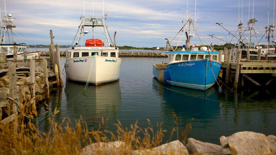 Two boats docked at a pier with a rocky shoreline and calm water.