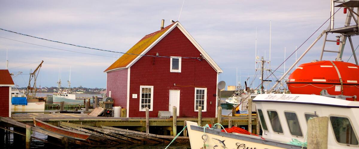 A red building with a white door and windows, a dock with boats, and a clear sky.