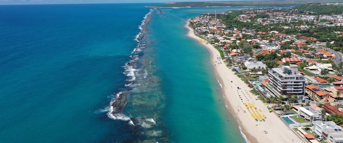 A coastal town with a long beach, clear blue waters, and a dense residential area with colorful buildings.