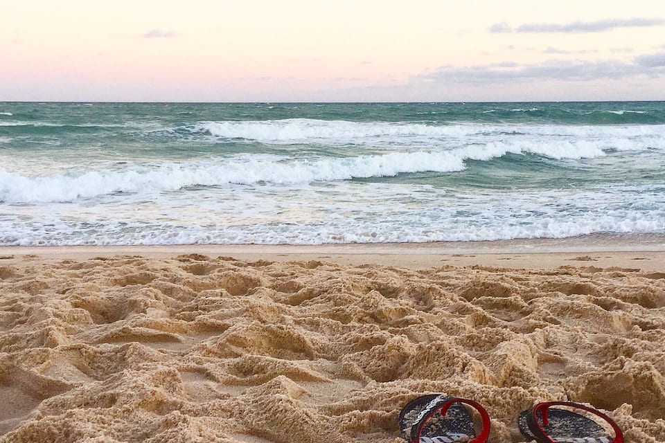 Une plage avec des vagues et une paire de tongs sur le sable.