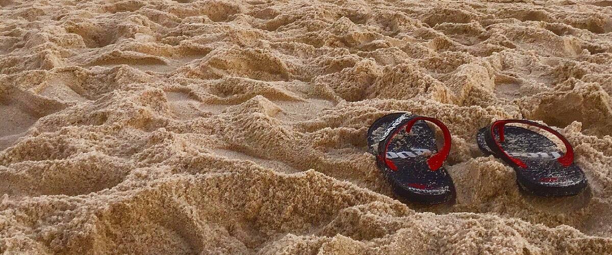 A beach with waves and a pair of flip-flops on the sand.
