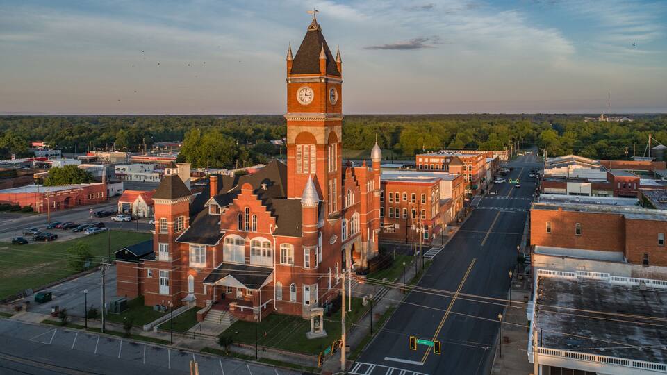 A historic building with a clock tower, surrounded by a town with streets and buildings.