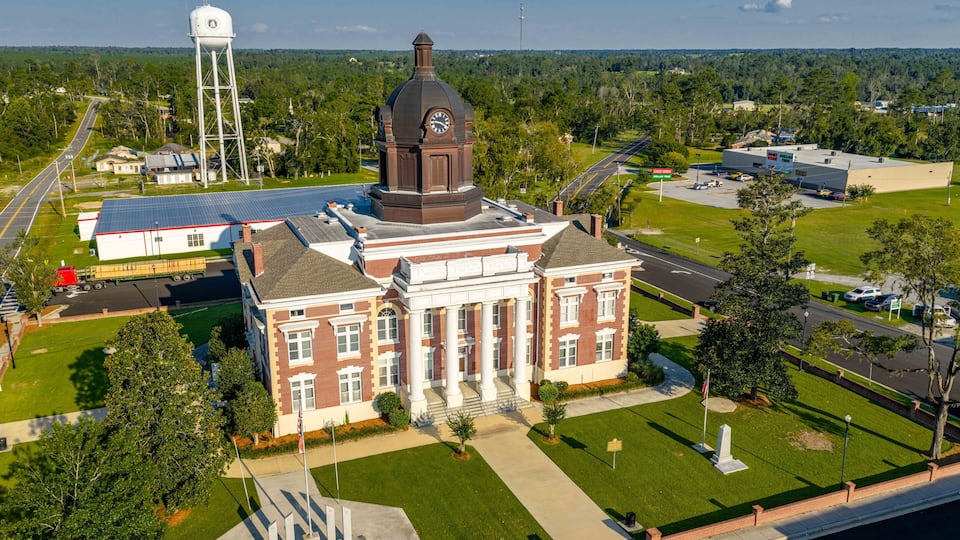 A large brick building with a clock tower, surrounded by green lawns and a water tower.