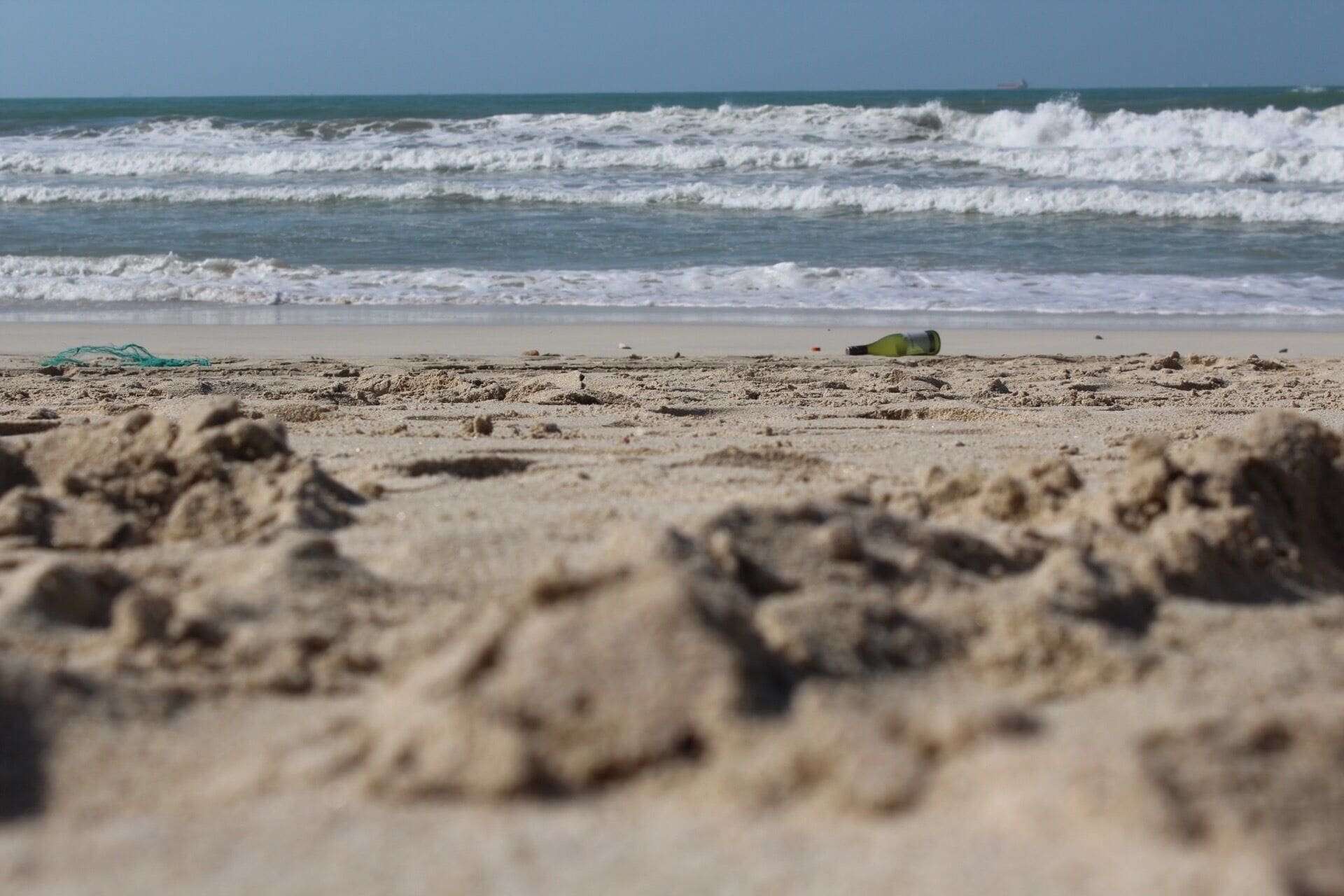 Una playa arenosa con olas rompiendo en la orilla y una botella verde sobre la arena.