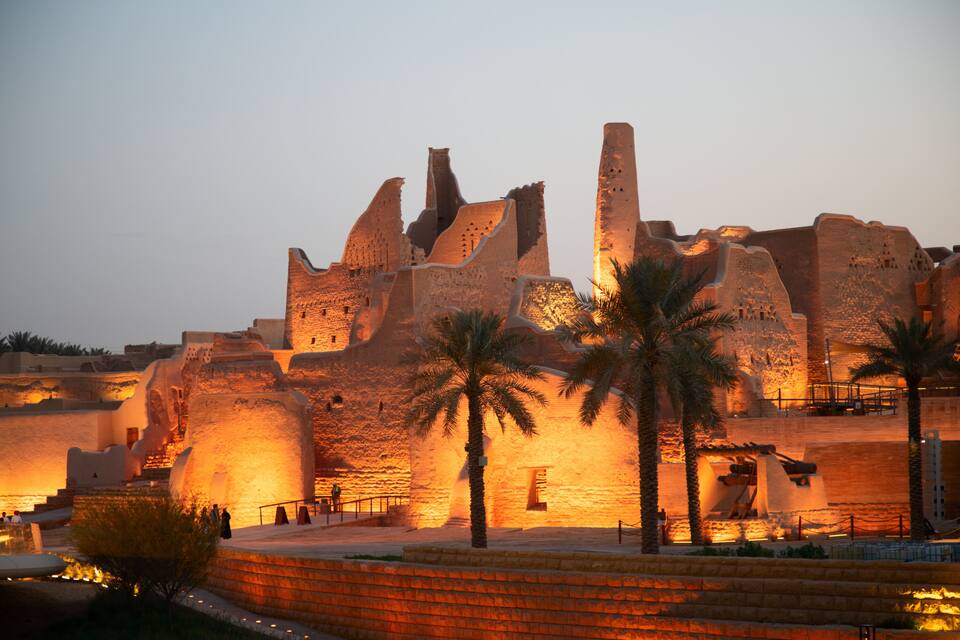 An ancient fortress with large stone walls and palm trees in the foreground.