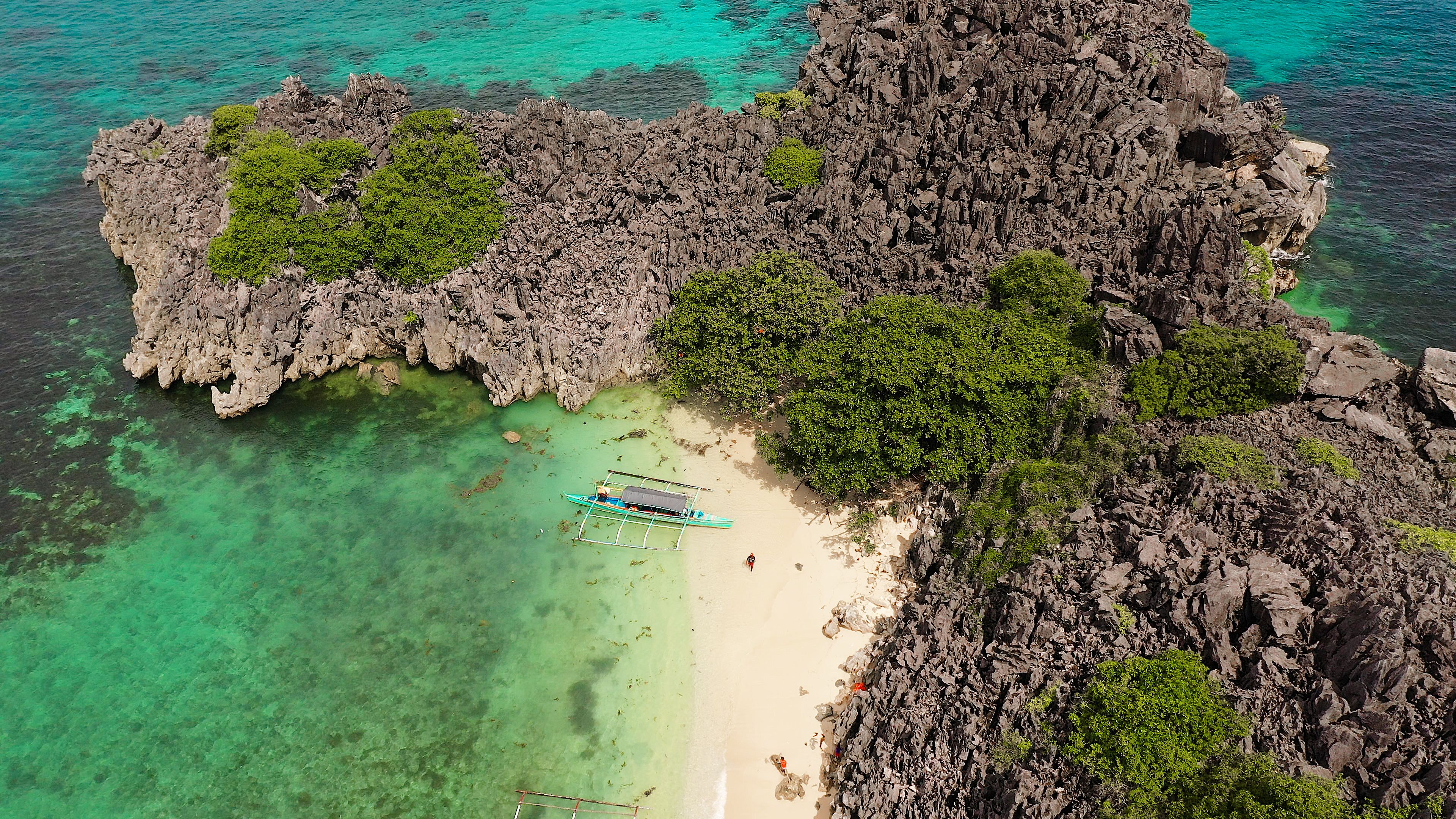 A rocky island with clear turquoise waters and a small boat on the beach.