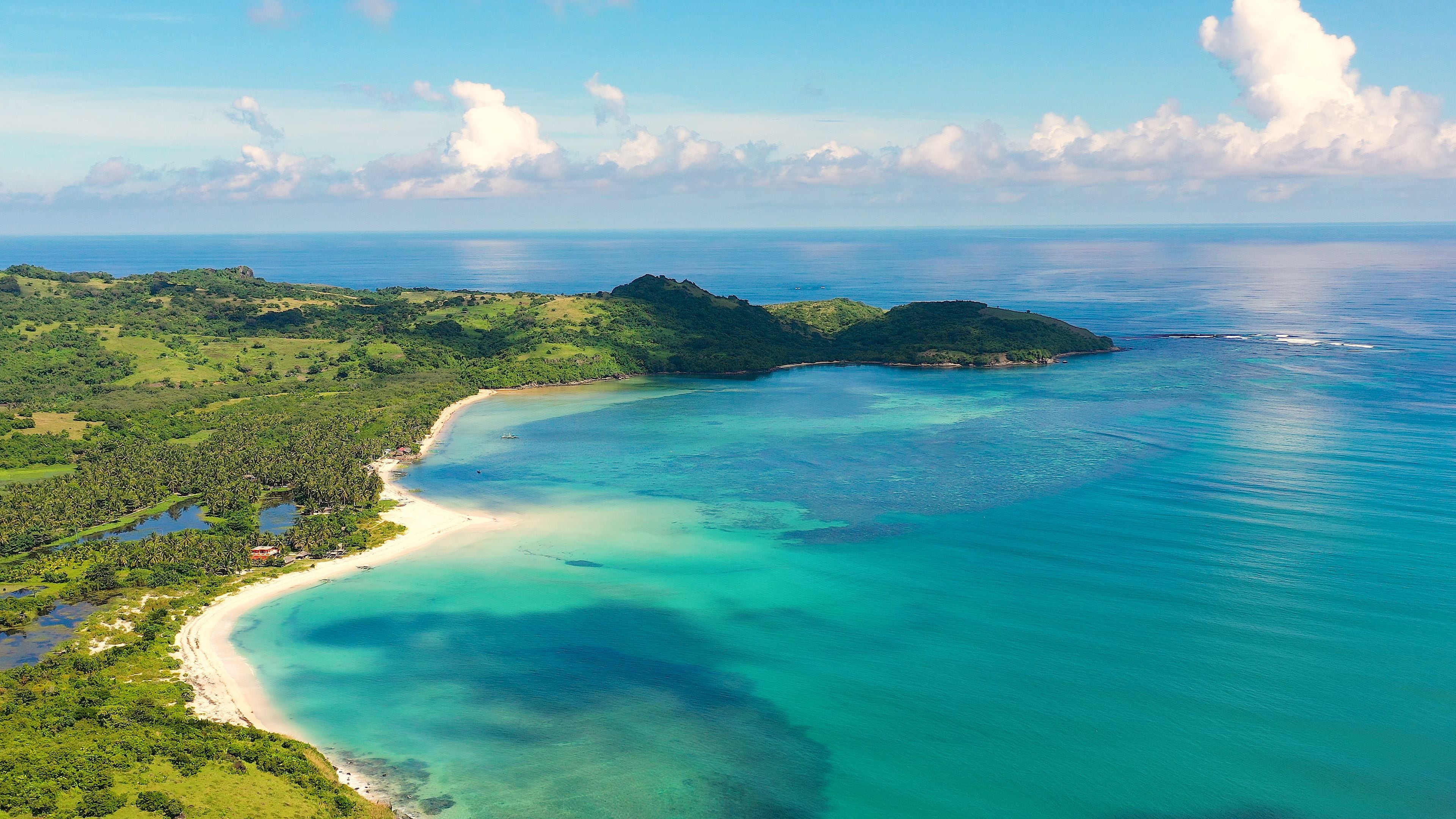 A coastal landscape with a sandy beach, clear turquoise waters, and lush green hills.